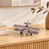 Avion décoratif en métal argenté sur une console en bois clair, avec livres, cadre et vase
